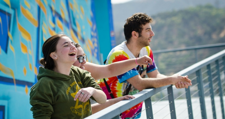 Image of laughing students standing in front of colorful mural on AJU campus