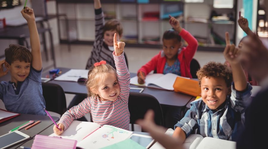 Photo of kids in classroom raising their hands