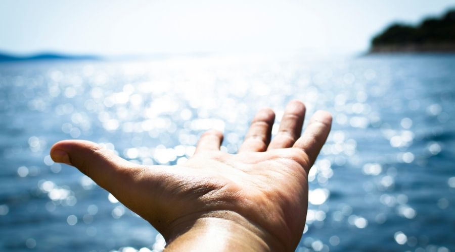 a hand held out over a body of water