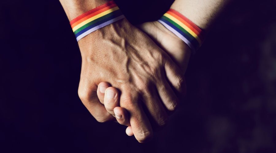 two hands holding wearing rainbow bracelets