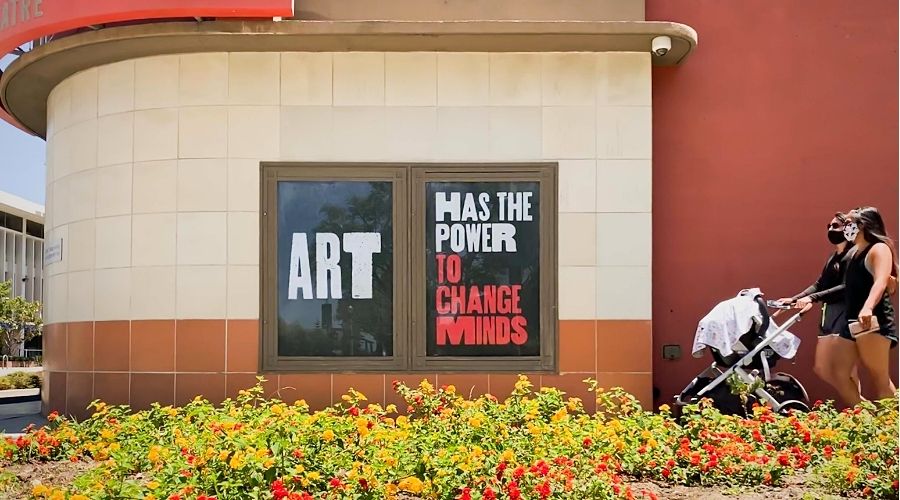 two masked people walking by a sign that says Art Has the Power to Change Minds