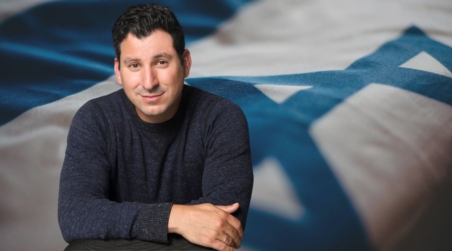 Noam Weissman sitting in front of an Israeli flag