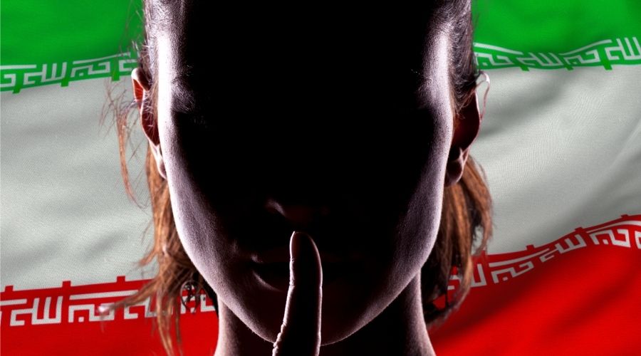 person with a finger on their lips in front of an Iranian flag