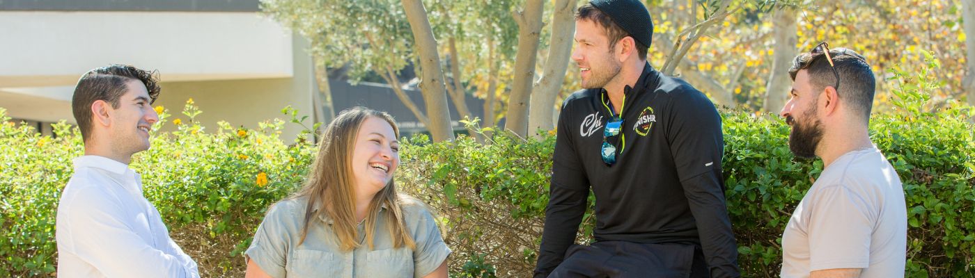 Four Ziegler Students, three men and one woman in the courtyard smiling at one another