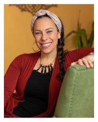 Headshot of Yael Eckstein Wearing a Red Sweater and black top sitting on a green chair in front of a yellow wall