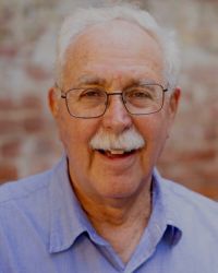 Headshot of Fredric Brandfon in blue shirt and with glasses