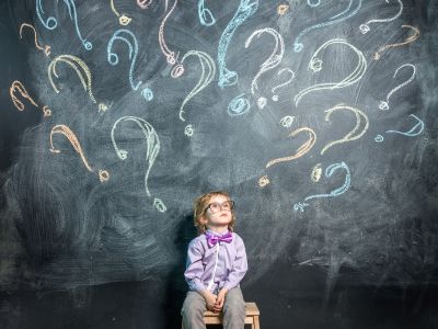 child looking up at blackboard with question marks