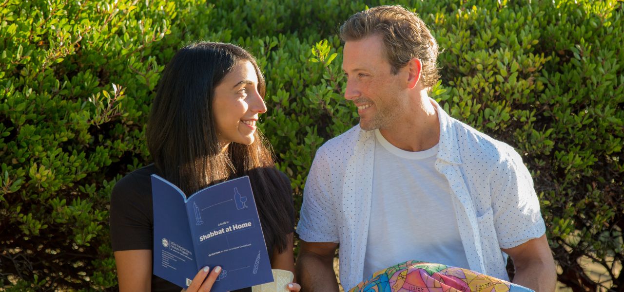 A couple smiling at each other holding challah and a text book