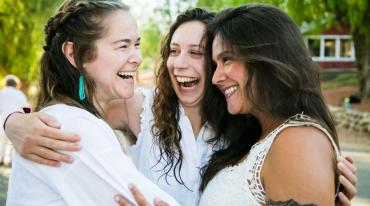 Photo of three women dressed in white embracing each other