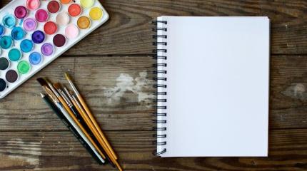watercolors and brushes next to a blank notebook